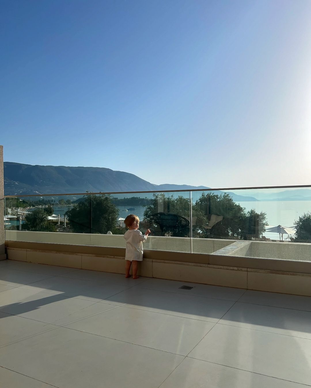 a little girl stands on a balcony overlooking the ocean