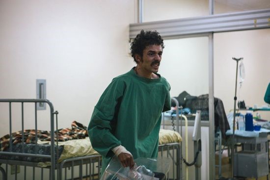 a man in a green gown is standing in a hospital room .