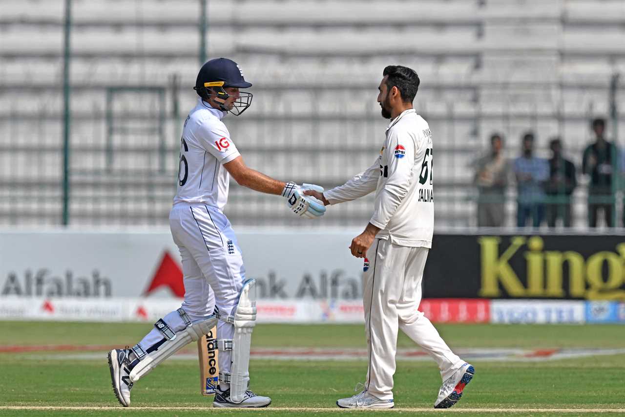 two cricket players shake hands on a field with an alfalah ad in the background