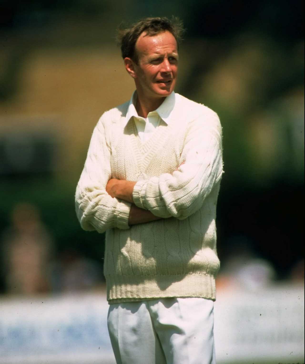 a man in a white sweater stands with his arms crossed