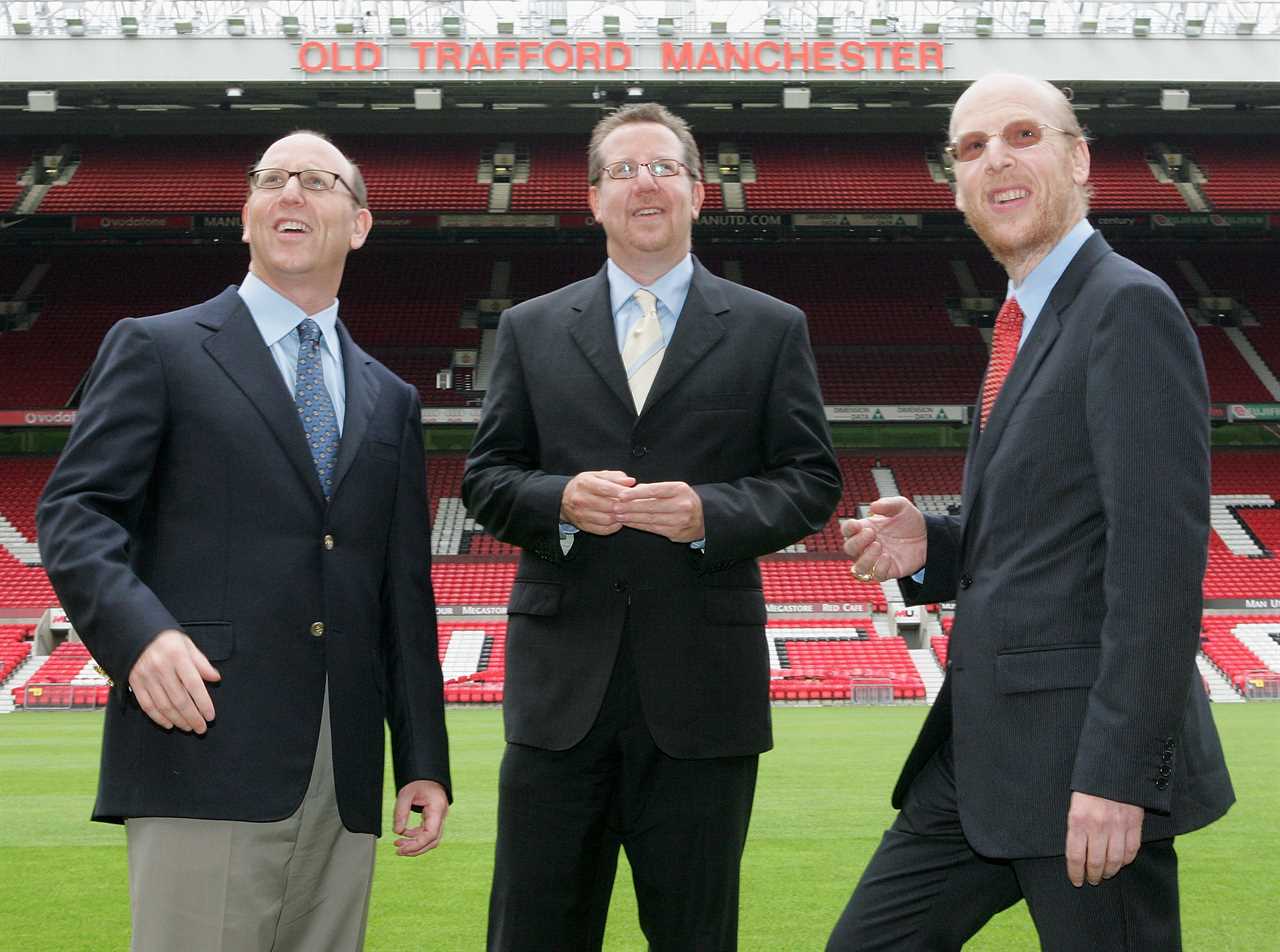 three men stand in front of an old trafford manchester stadium