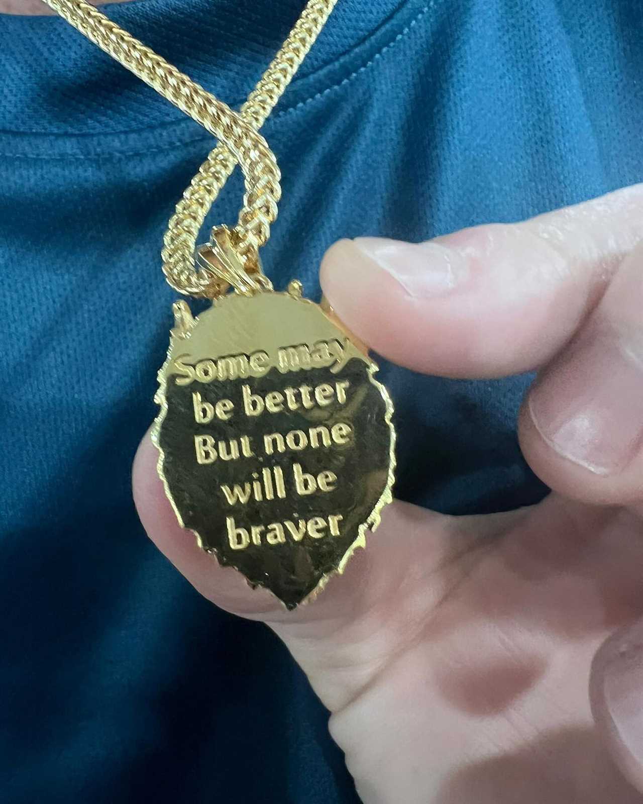 a person is holding a gold necklace that says some may be better but none will be braver