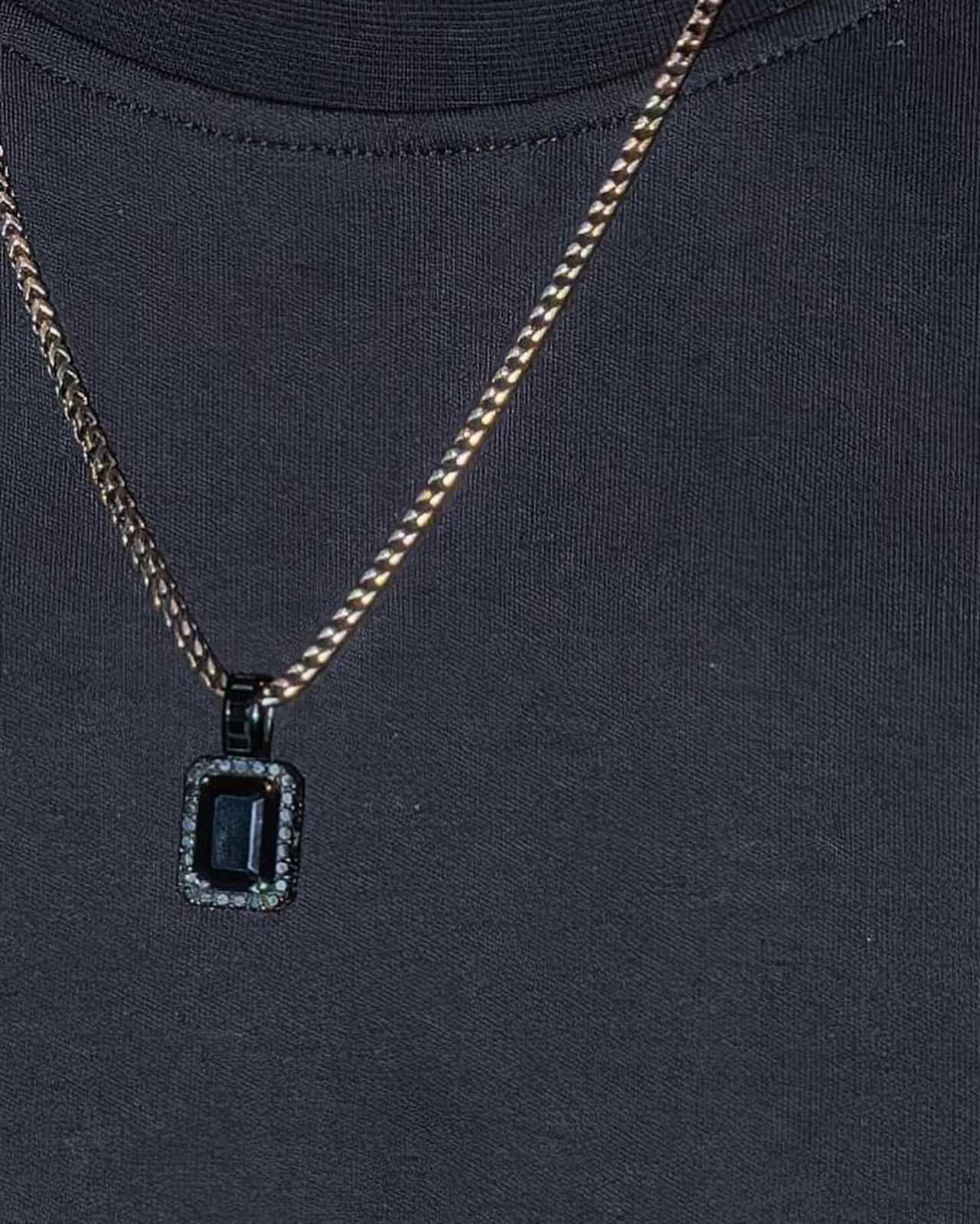 a close up of a necklace with a square pendant on a black shirt .