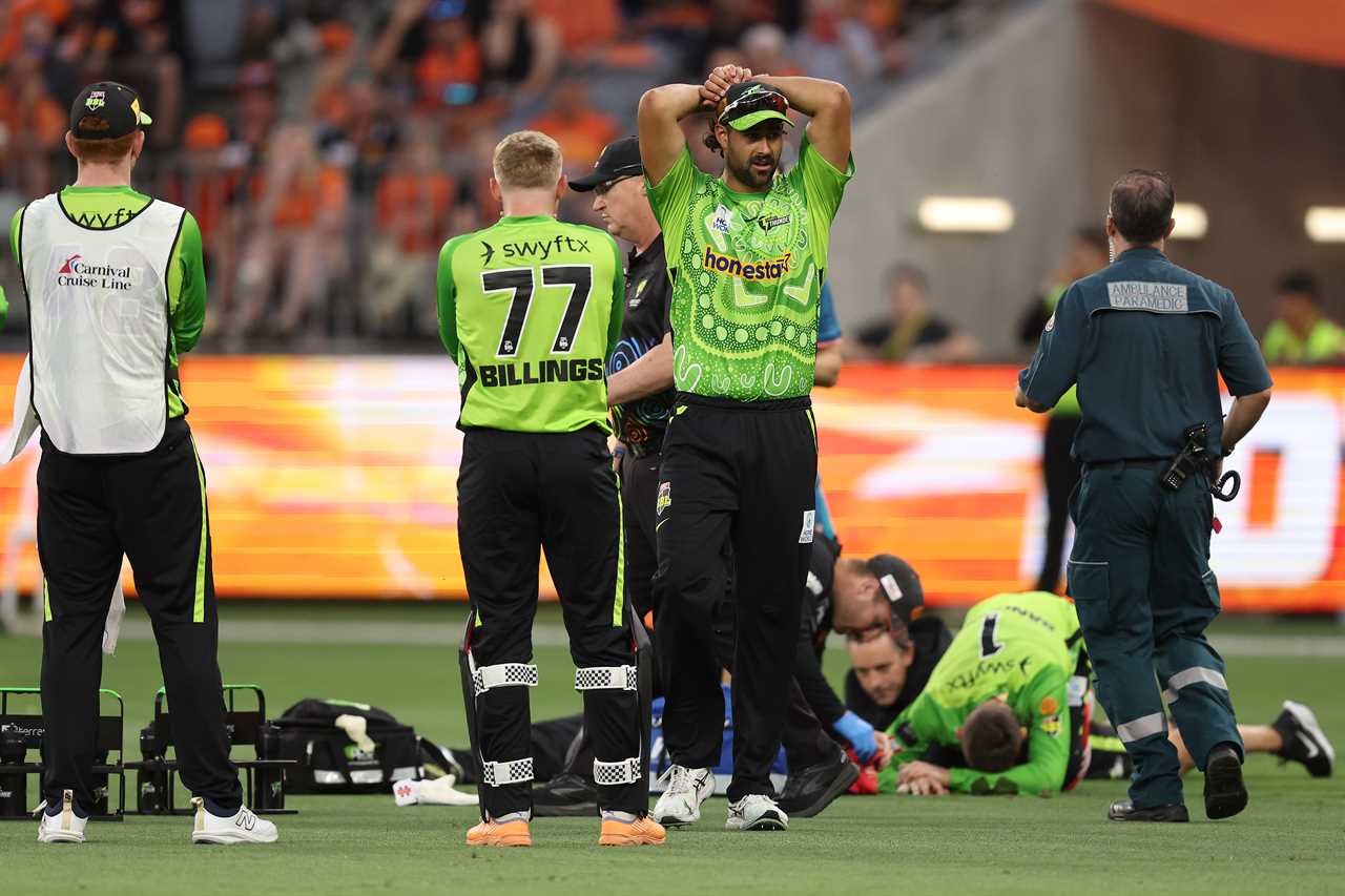 Cricket player Wes Agar watches as medical staff attend to injured teammates.