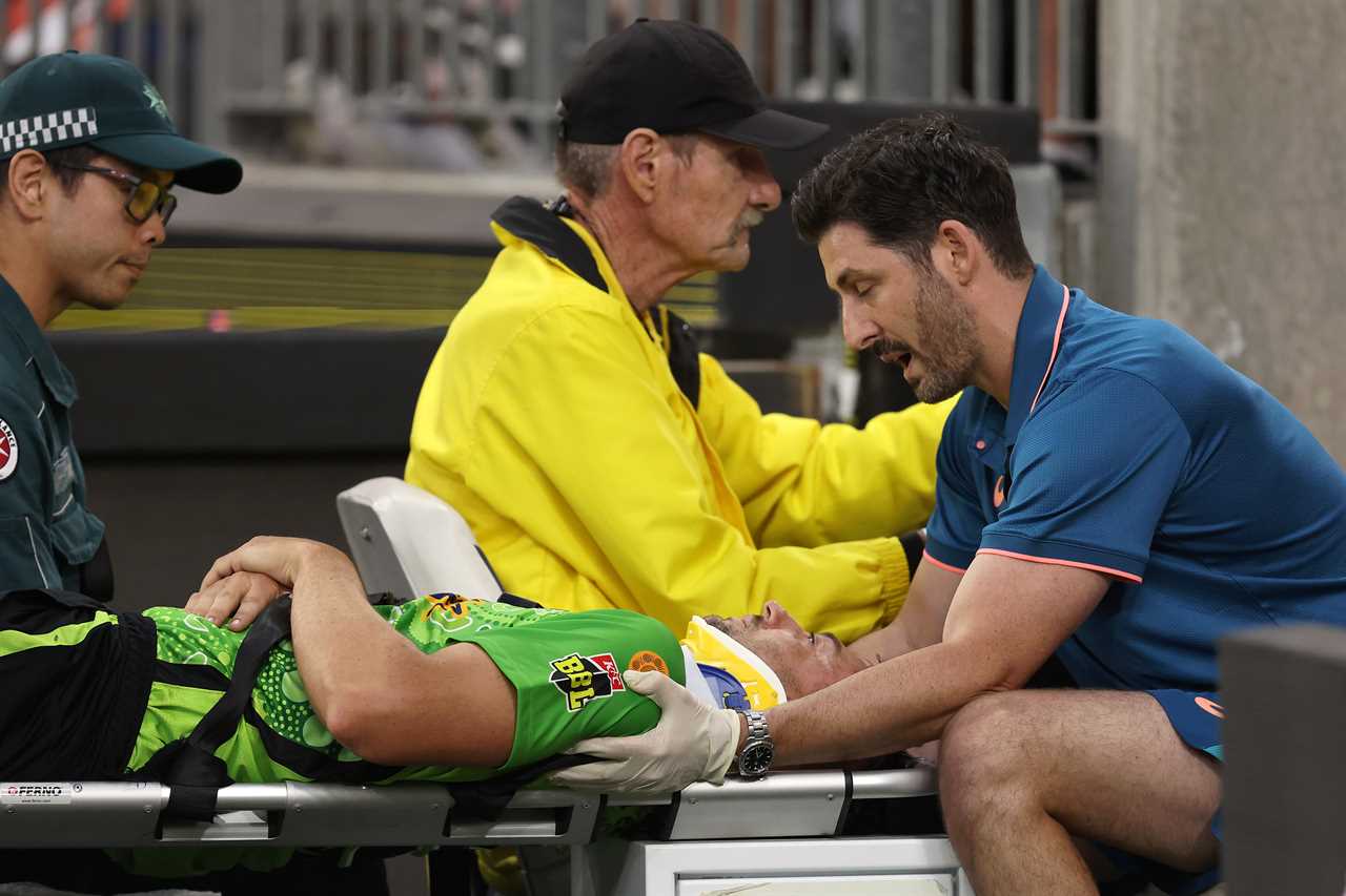 Injured cricket player being carried off the field on a stretcher.