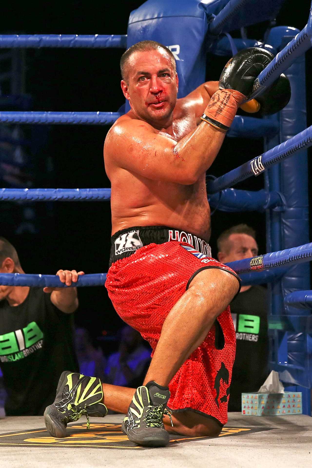 Boxer Adam Hollioake kneeling in a boxing ring after a match, bleeding from the nose.