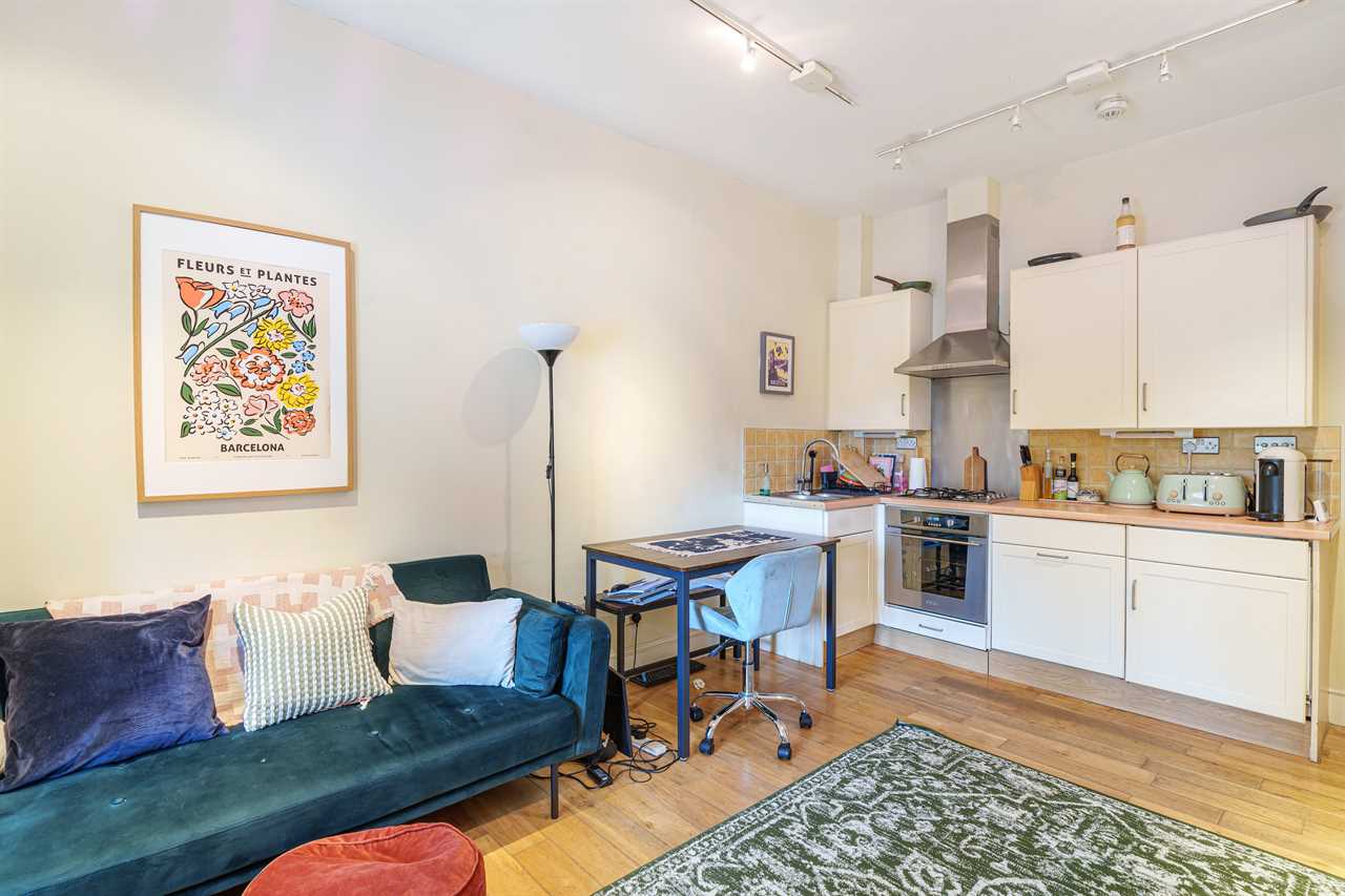 Open-plan living room and kitchen with teal sofa and small dining area.