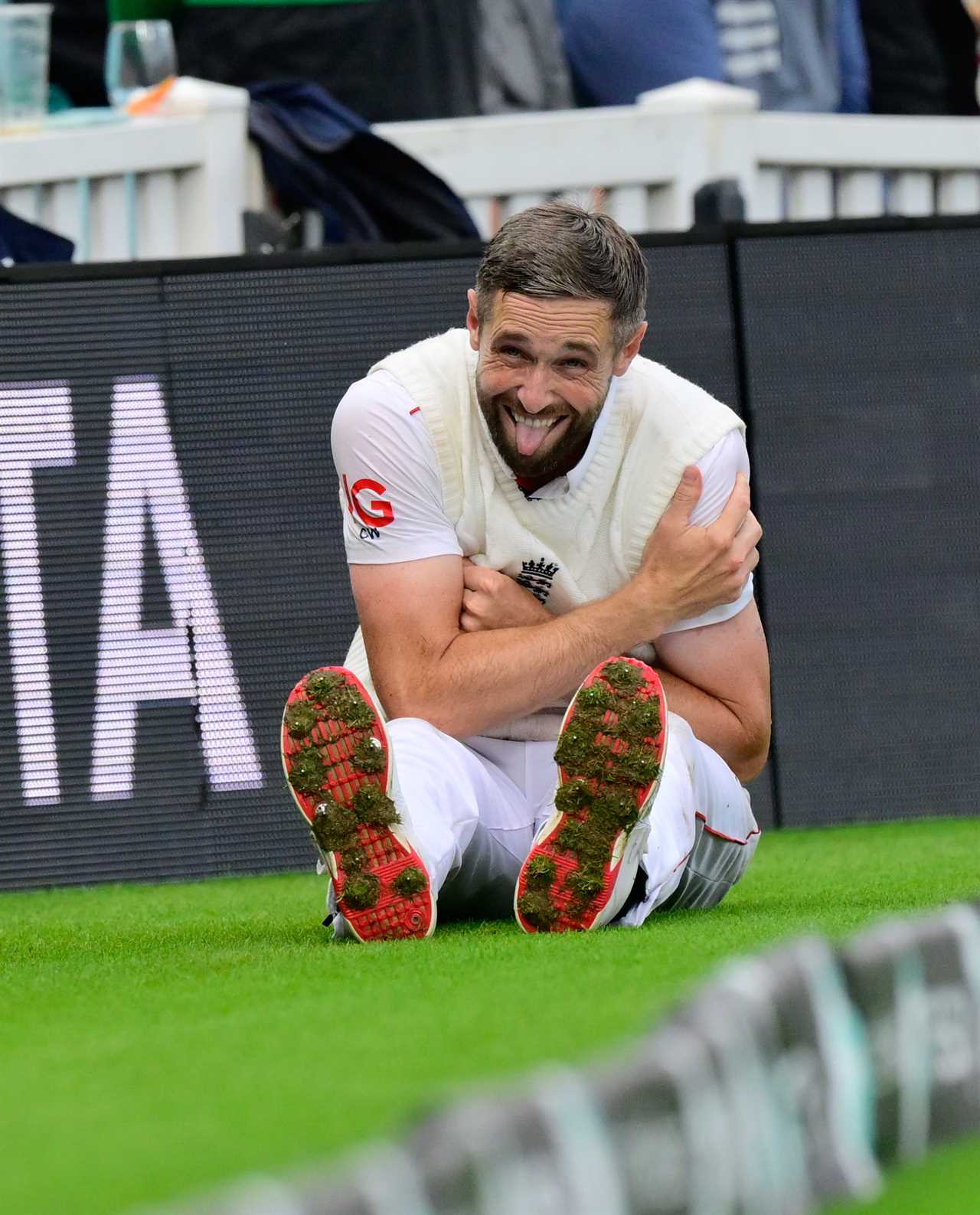 Chris Woakes of England sitting on the ground, holding his injured shoulder and sticking his tongue out.