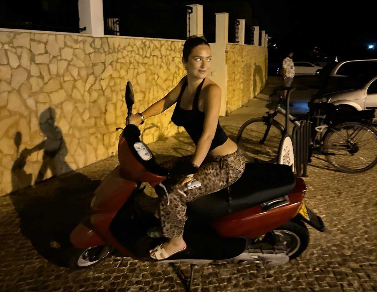 Woman sitting on a red scooter at night.