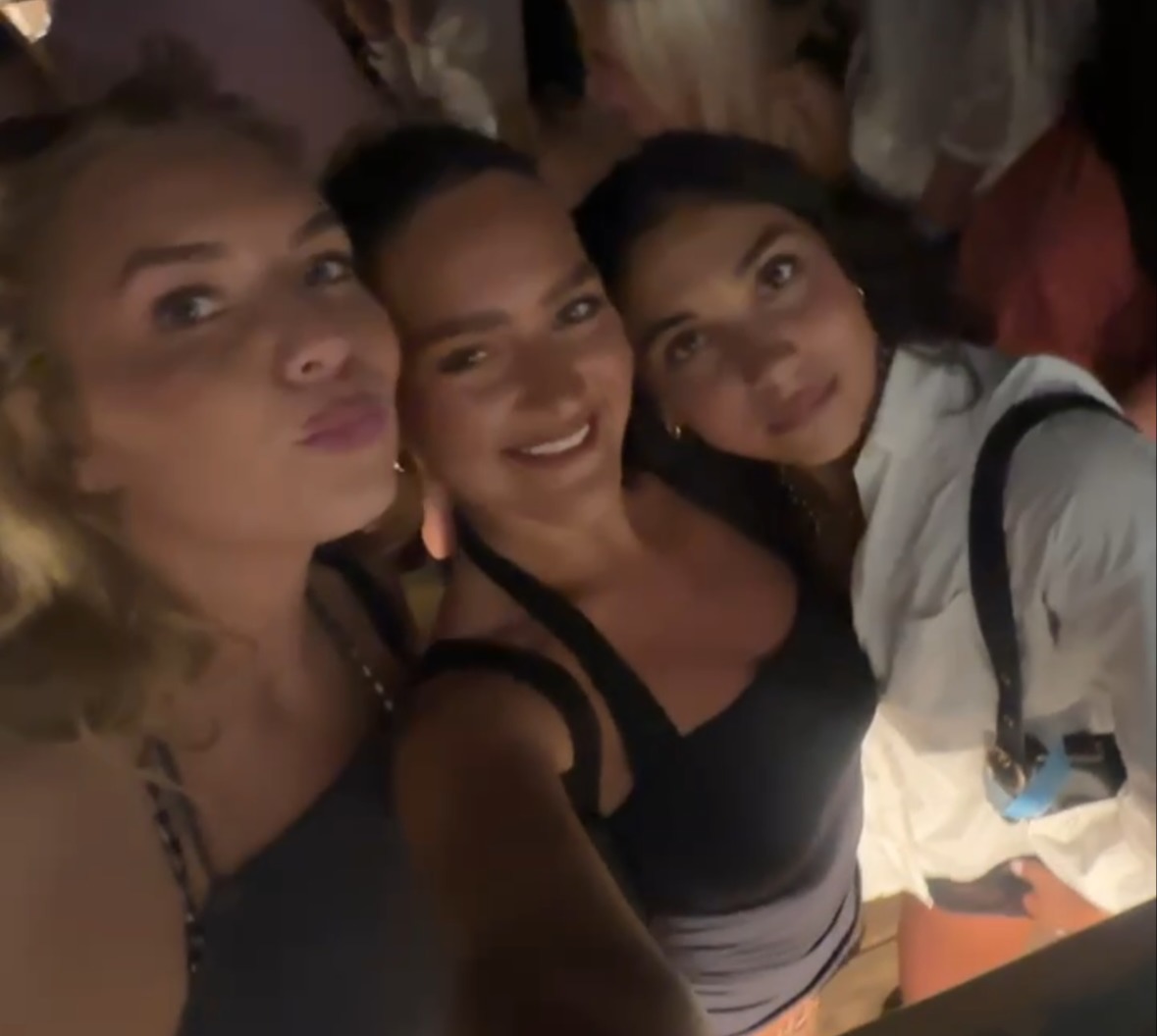 Three women posing for a selfie at a crowded nightclub.